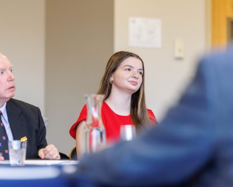 Two people seated at a table in a meeting room, with a glass pitcher and papers in front of them.