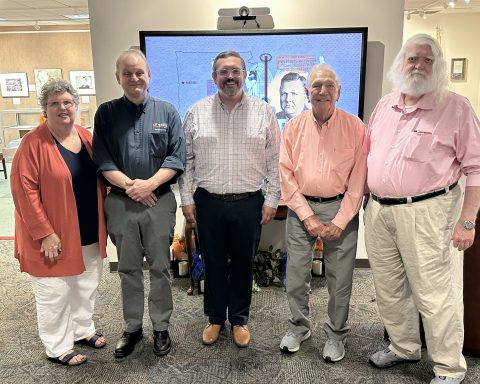 Five people are posted in front of a projection screen.