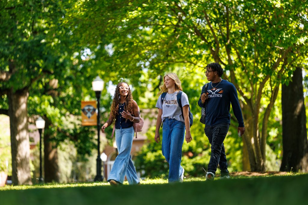 Three students are walking in a tree-shaded area of a campus