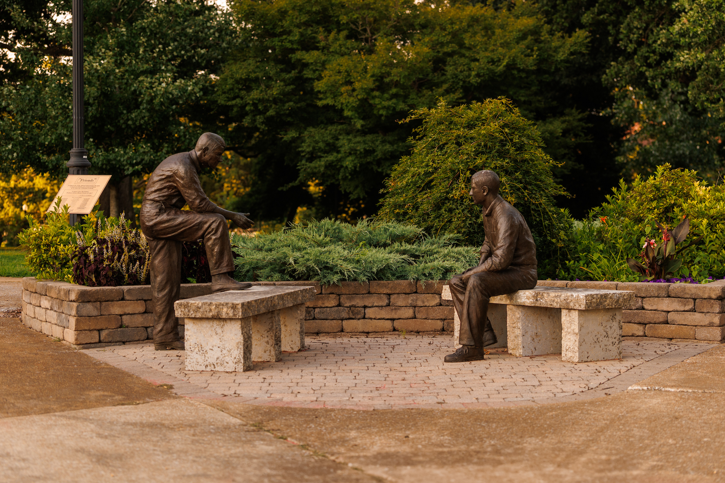 Statues of two men, one seated and one standing with his foot resting on a bench, are shown