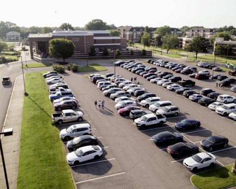 Several cars are shown in a full parking lot next to university buildings