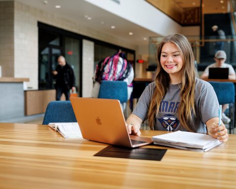 A female student smiles as she works on her laptop computer
