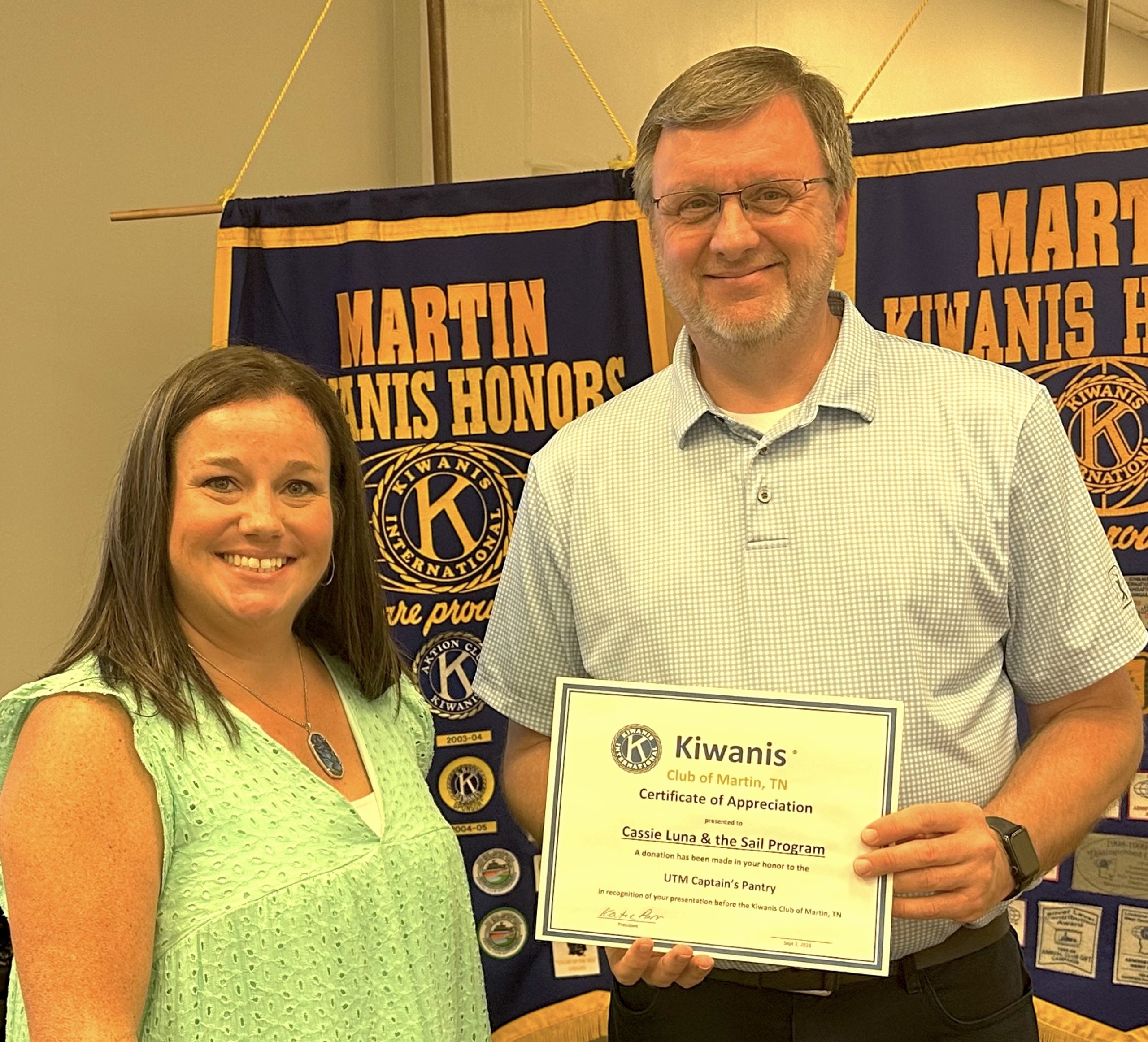 A woman and a man pose for a photo with the man holding a certificate