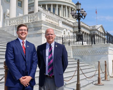 A young man and a legislator are posing on the steps of the U.S. Capitol