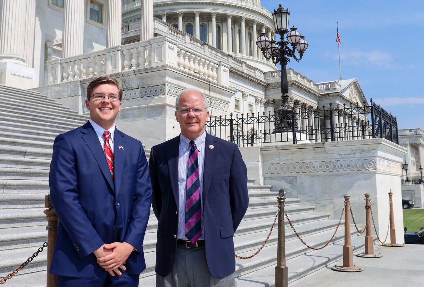 A young man and a legislator are posing on the steps of the U.S. Capitol