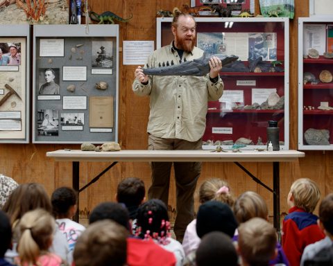 A man is shown holding a fossilize jawbone in front of a group of children