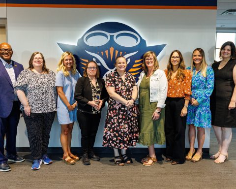 Nine people are posed in a line for a photo
