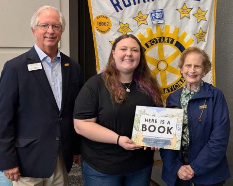 Three people are posed with one holding a book