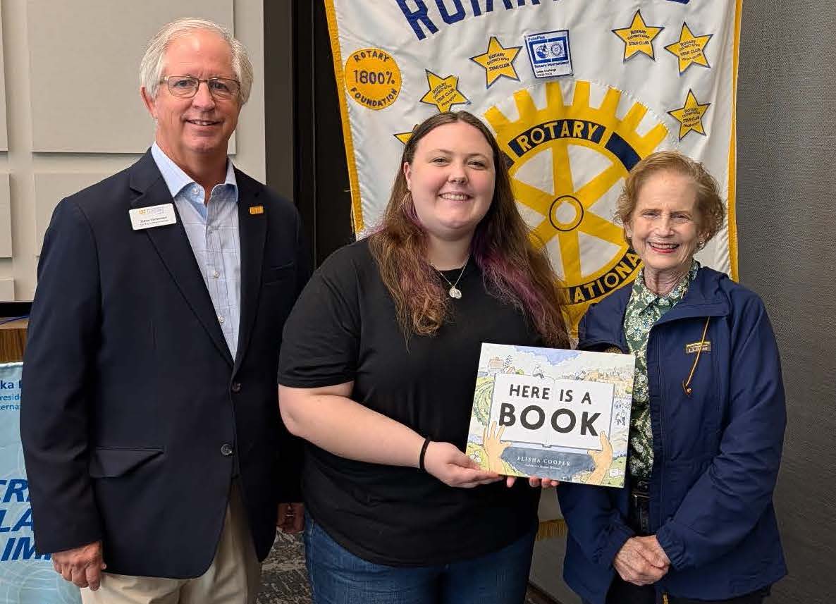 Three people are posed with one holding a book